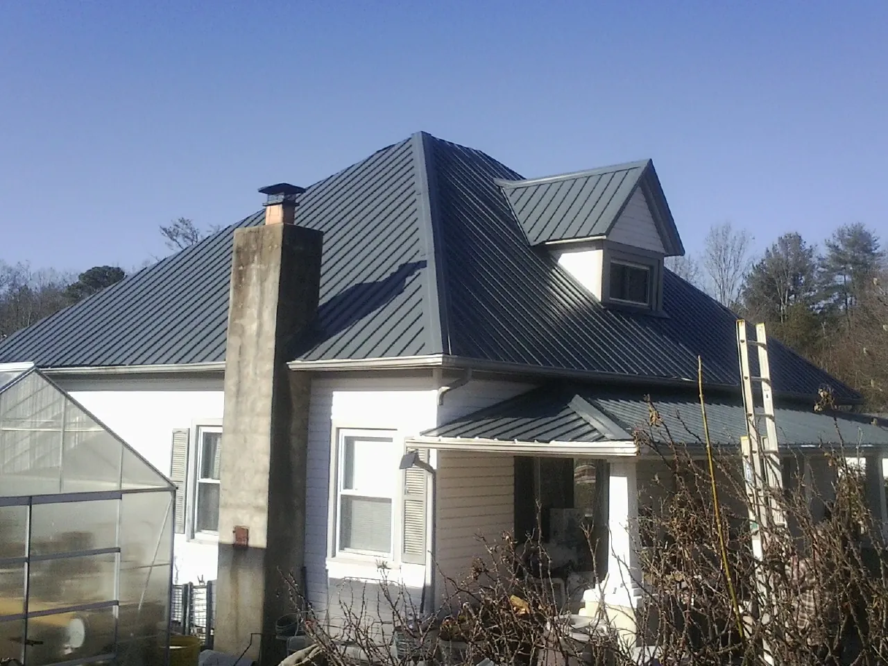 Dark blue standing seam metal roof on a white farmhouse with dormer — Slate & Tile Roof Repair by Roofing Brothers in James Creek