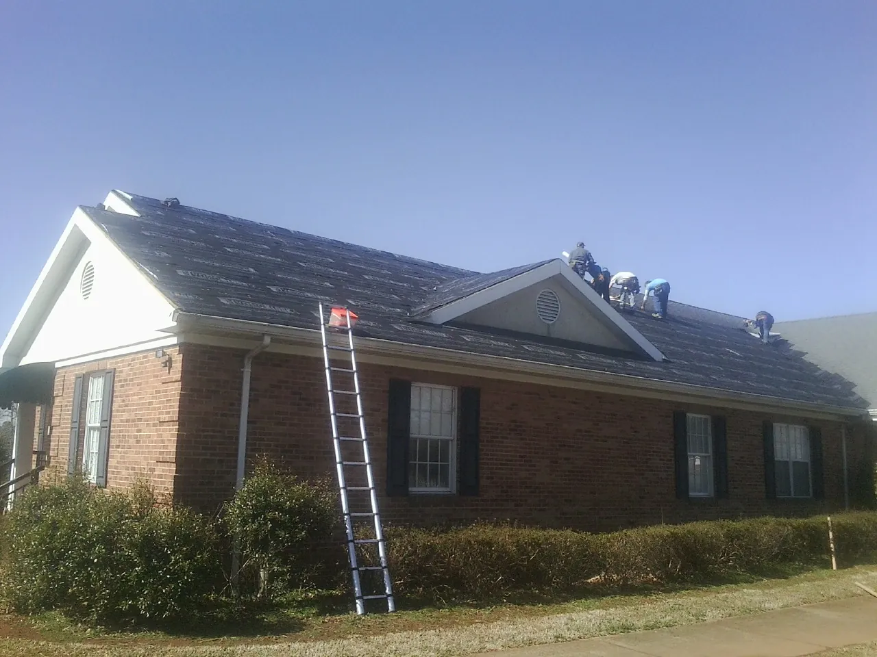 Crew tearing shingles off a brick ranch roof with a ladder set — Metal Roof Repair work by our crew in James Creek