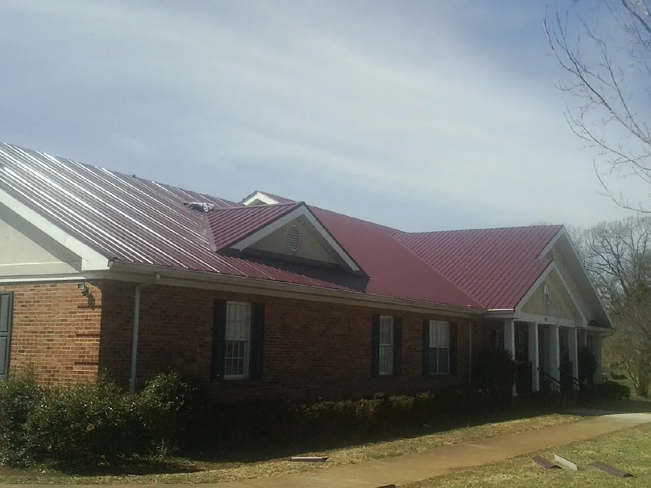 Red metal roof with gabled entries on a long brick building, from a Hail Damage Roof Repair job in James Creek