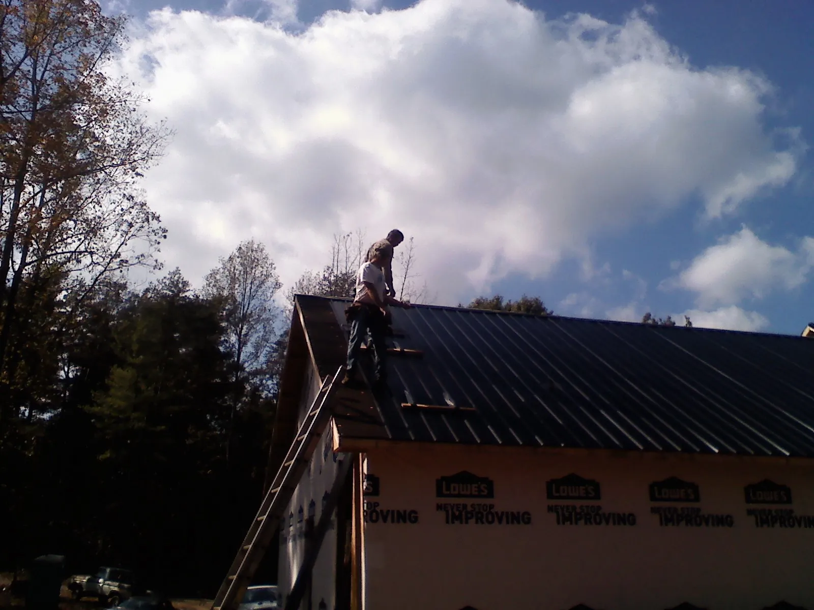 Roofer fastening dark metal panels high against a cloudy sky, from a Roof Inspection job in James Creek