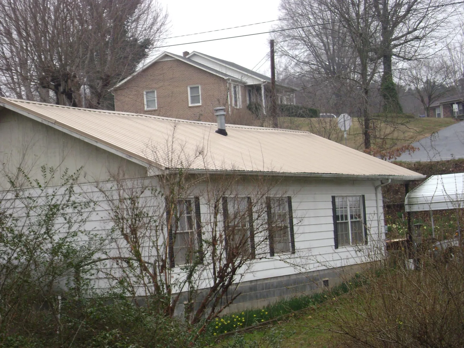 Tan metal roof on a white sided house set into a hillside — Commercial Roofing by Roofing Brothers in James Creek