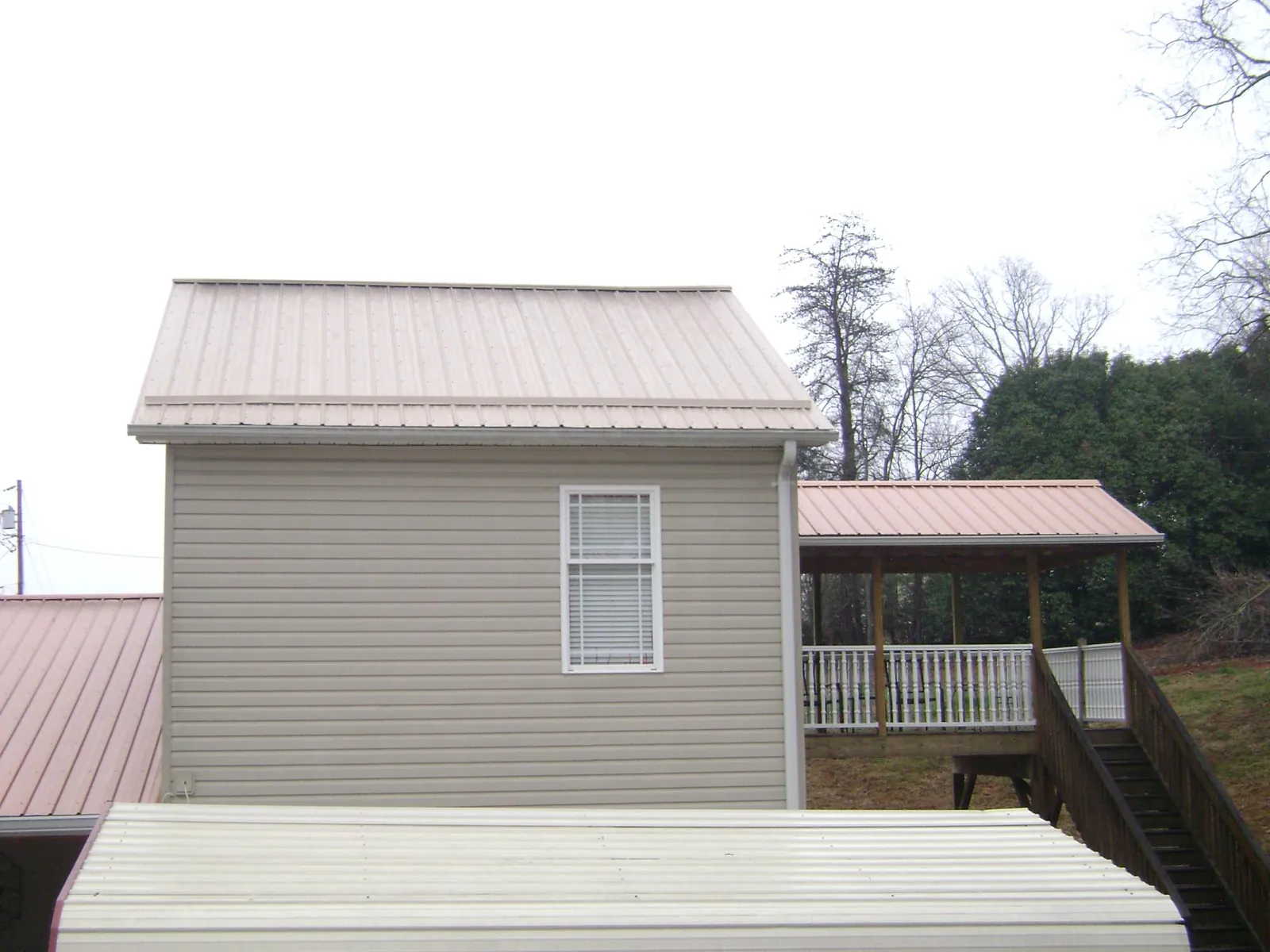 Tan metal roofs on a two story addition and attached porch, from a Roof Replacement job in James Creek